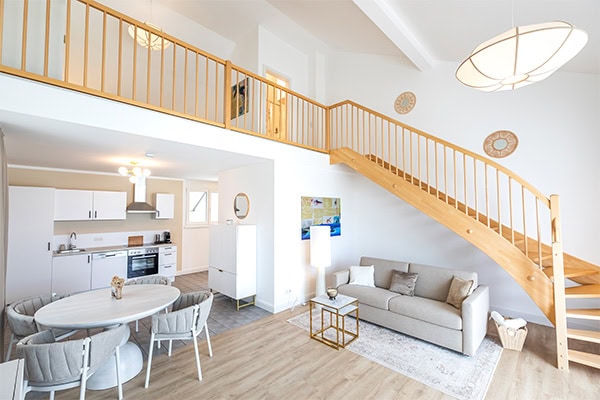 Ferienappartement Rocky Lake Heller offener Wohnraum mit Holztreppe und gemütlichem Sitzbereich.