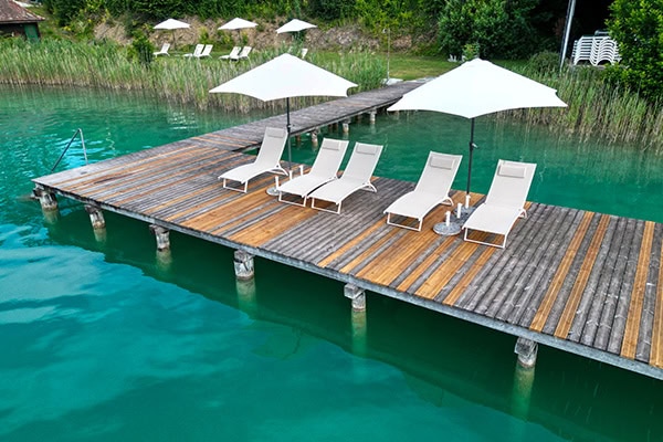 Der Sandwirth – Entspannungsbereich am Wasser Entspannungsbereich mit Liegen und Sonnenschirmen am Wasser.