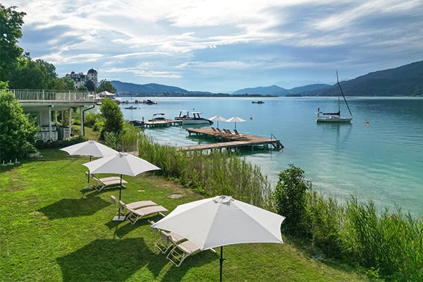 Der Sandwirth – Seeblick und Entspannung Entspannende Seeblick mit Liegestühlen und Sonnenschirmen am Wasser.